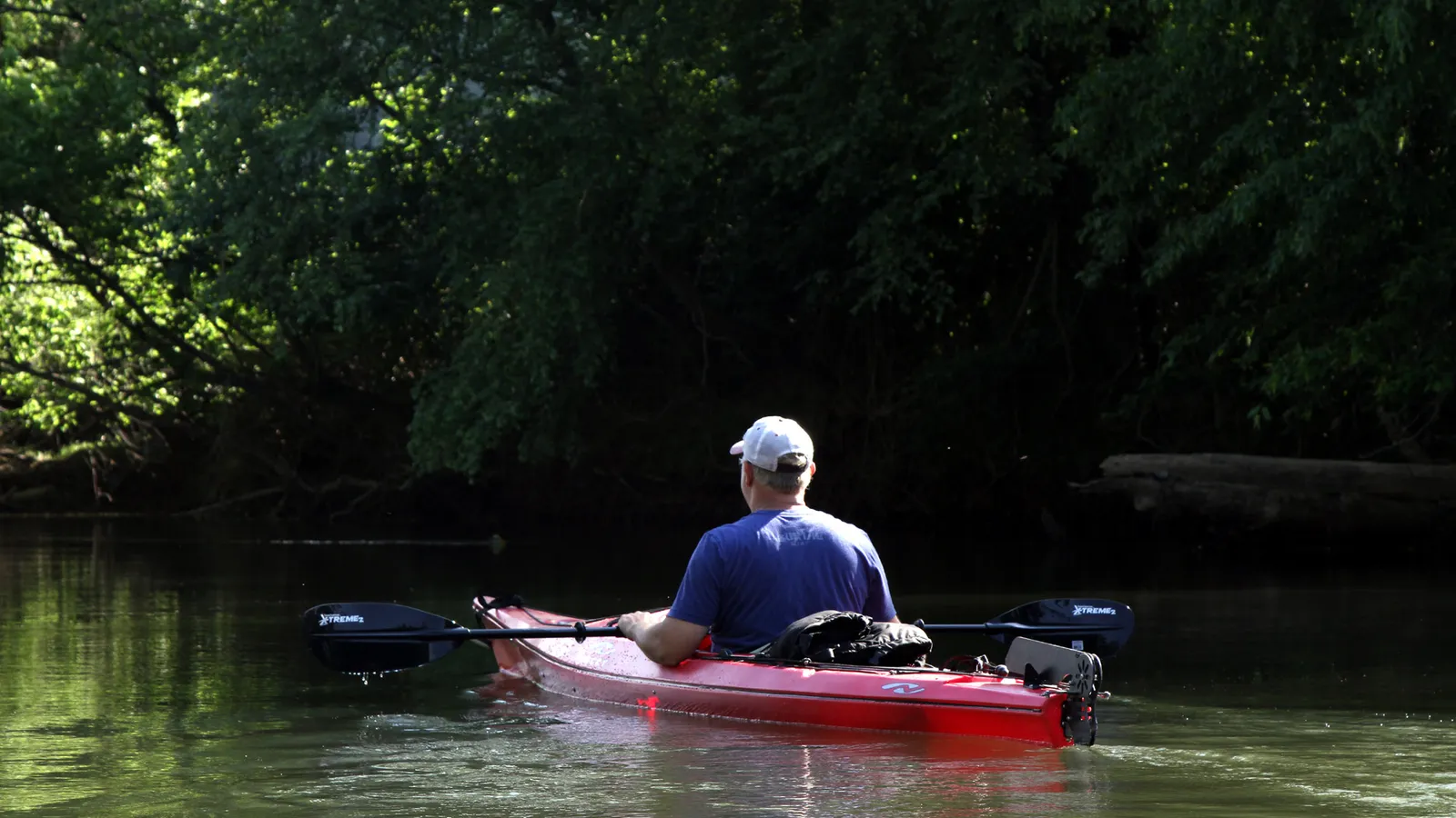 A kayaker floating a shady, flat stretch of the French Broad River through the Biltmore Estate