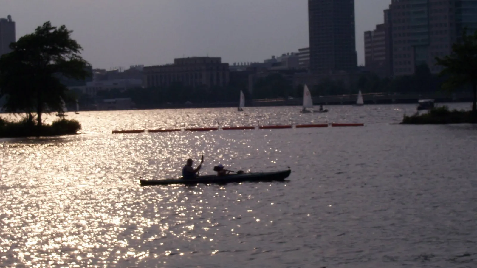 A kayaker on the Charles River by the Esplanade at sunset, with the city behind