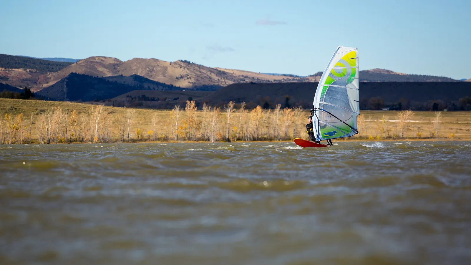 A windsurfer crossing choppy water on Boulder Reservoir, with brown foothills behind