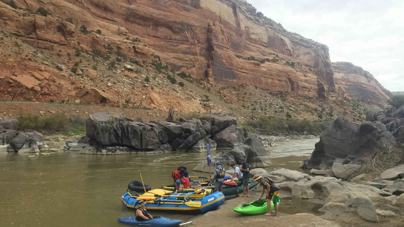 Rafts and kayaks pulled up on the bank of the Colorado River below red cliffs in Ruby Canyon