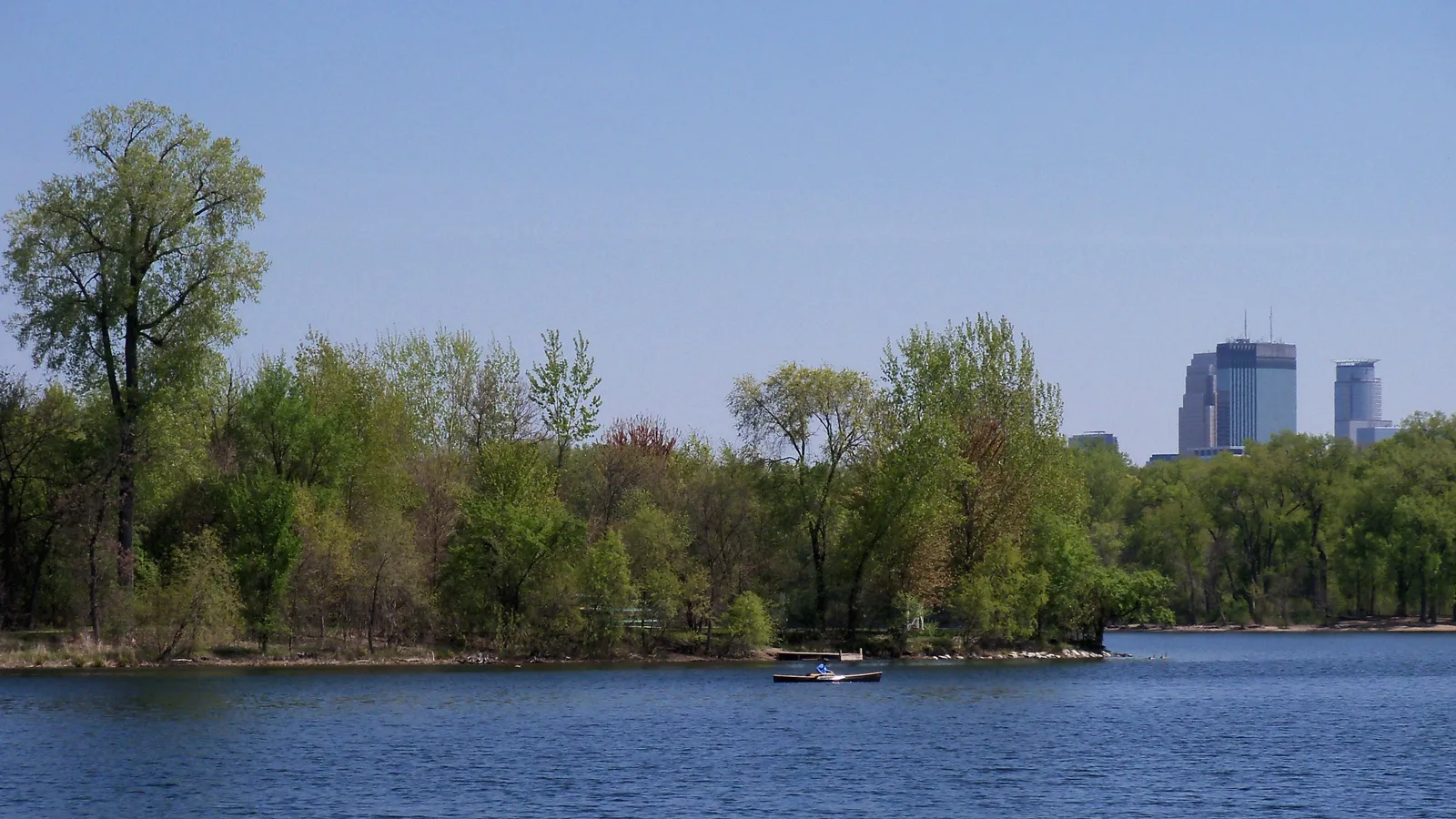 Cedar Lake with a wooded shoreline and downtown towers peeking over the trees