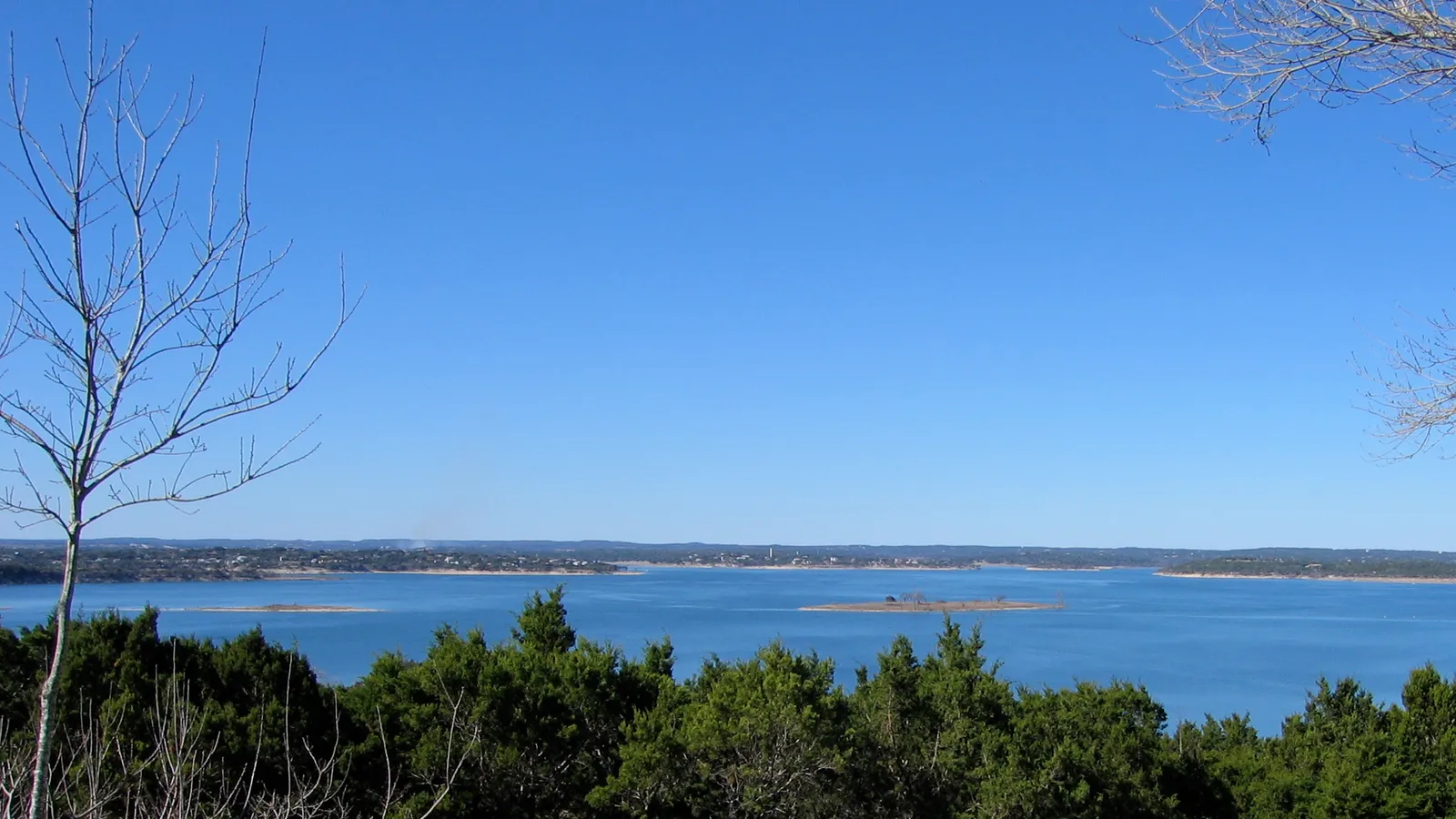 The wide main basin of Canyon Lake under a blue sky, seen from a wooded hill