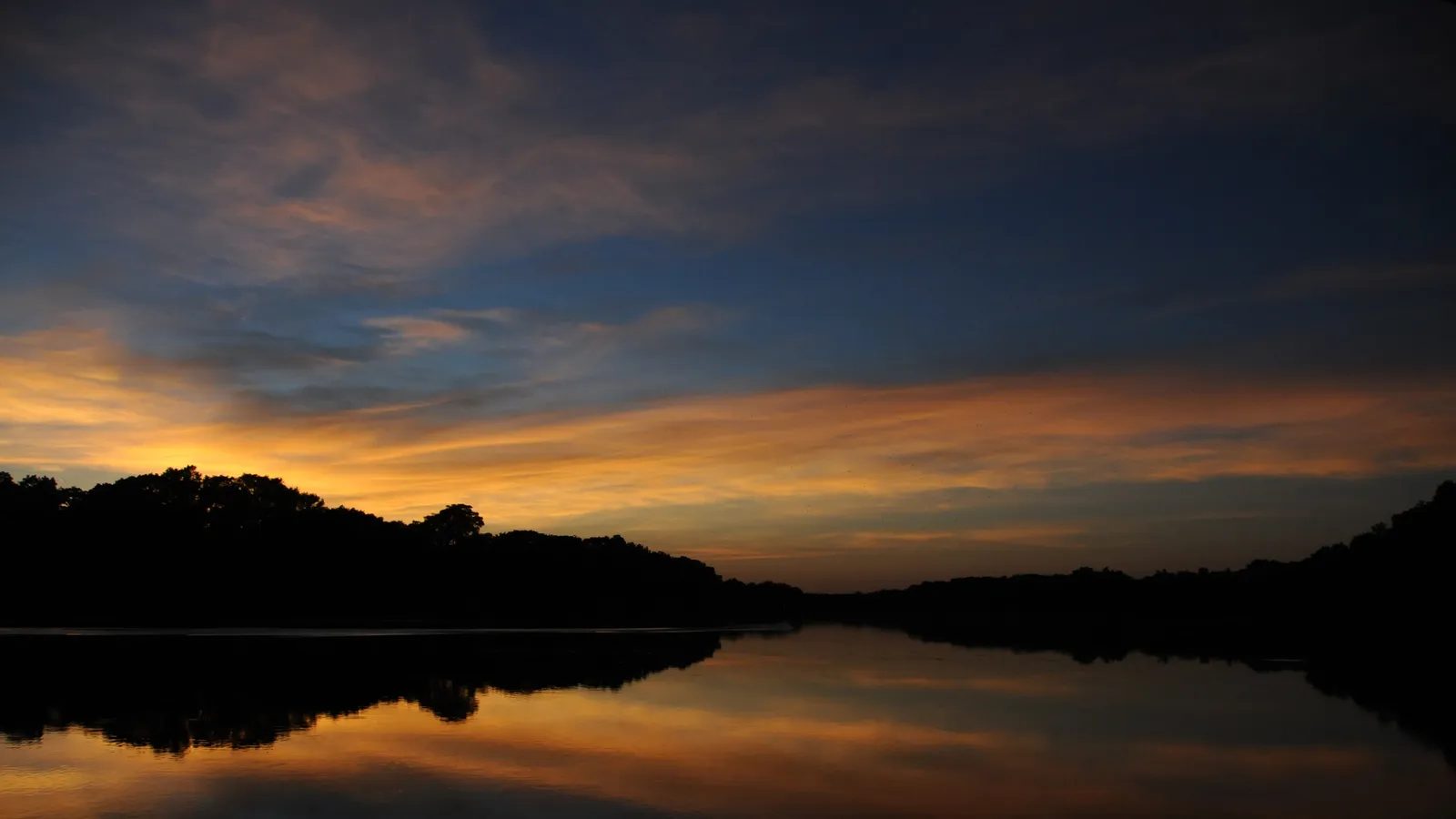 Sunset over calm water and wooded banks on Lake Dunlap