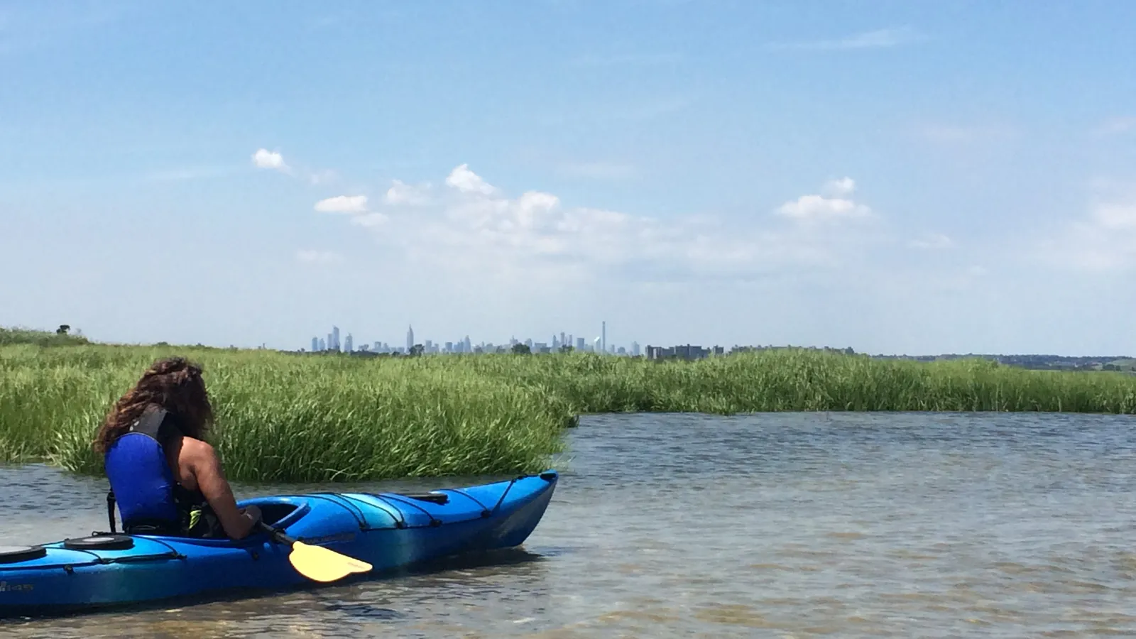 A kayaker beside a salt marsh in Jamaica Bay, with the Manhattan skyline far in the distance