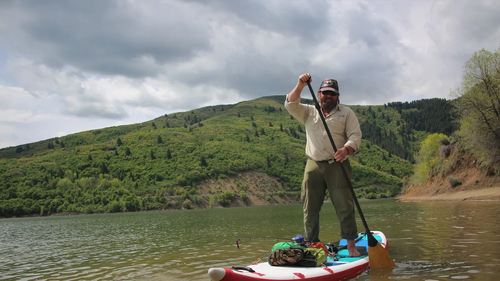 A paddle boarder on Pineview Reservoir below green hills in Ogden Valley