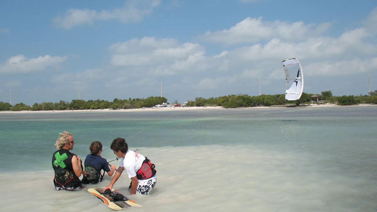 People sitting in ankle-deep water on the sand flats off Anne's Beach, with a kite in the distance