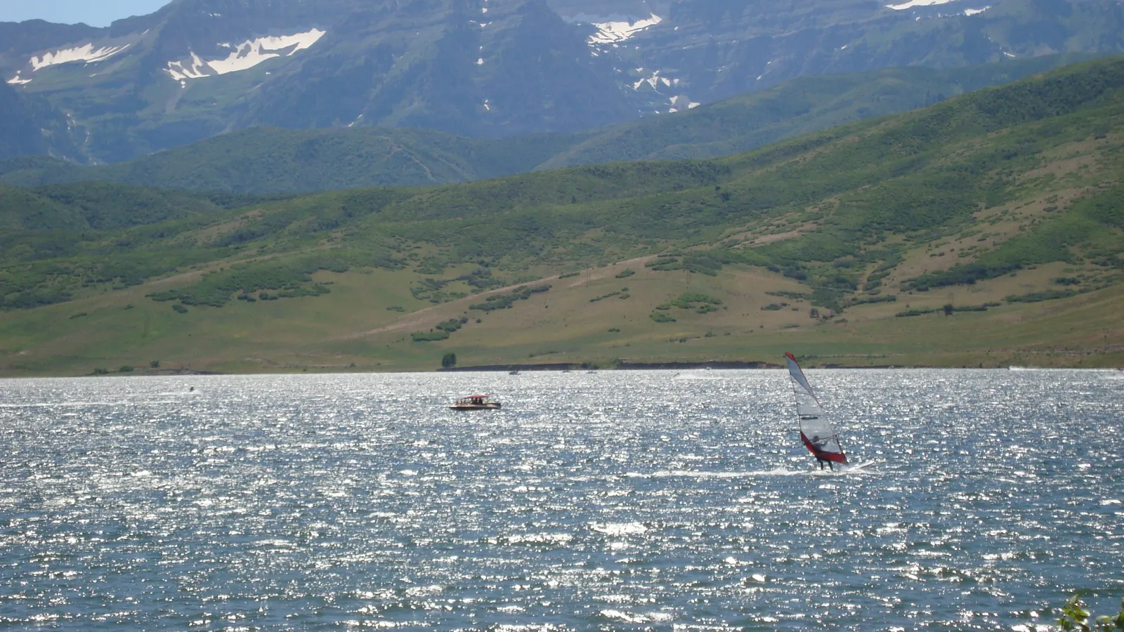 A windsurfer and a boat on Deer Creek Reservoir below green hills