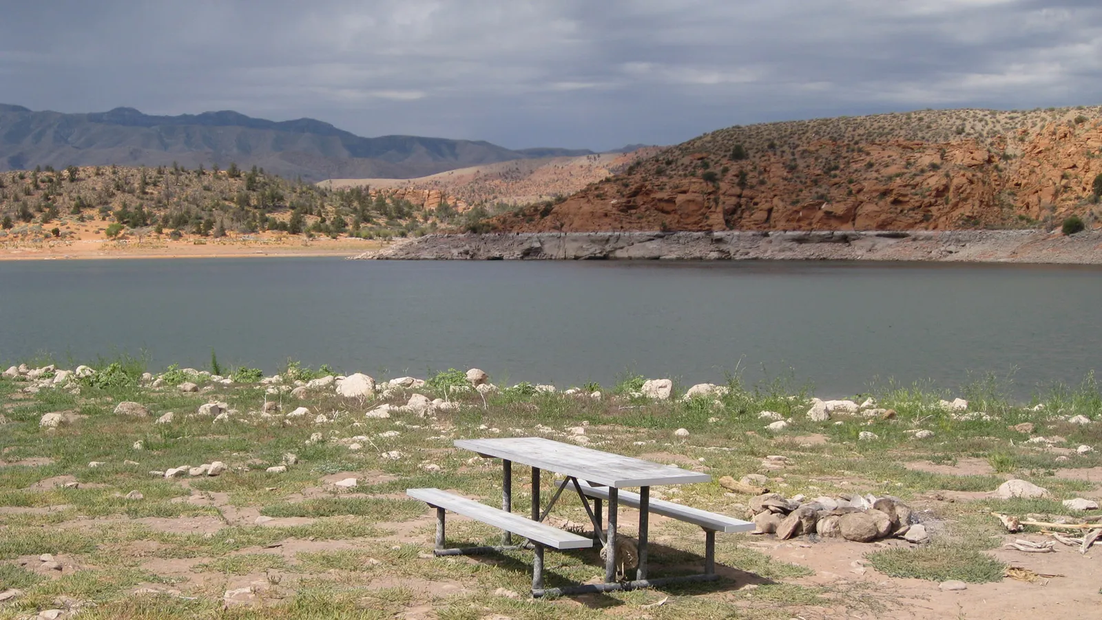 A picnic table on the shore of Gunlock Reservoir, with red rock hills across the water