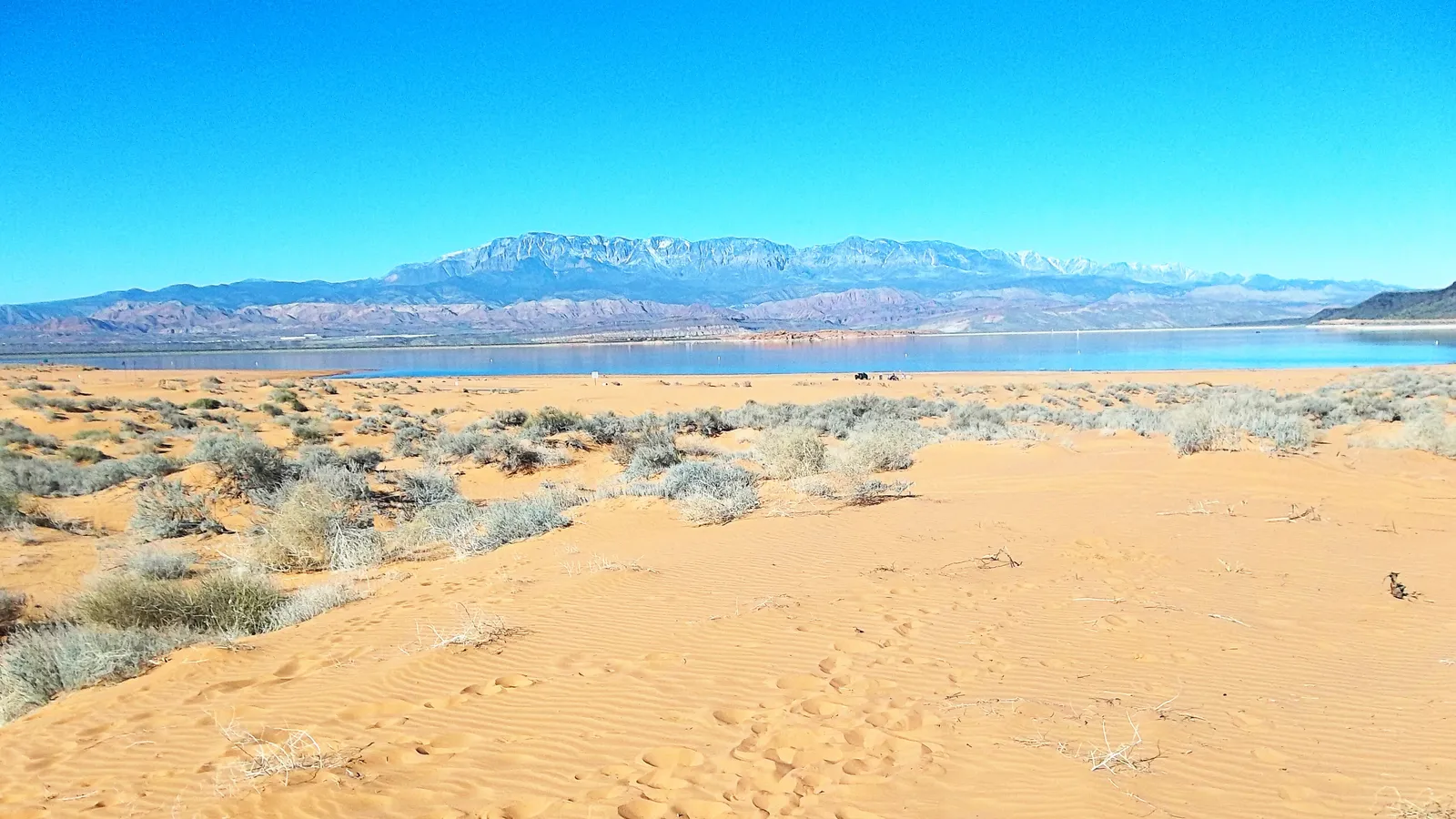 Rippled sand on the shore of Sand Hollow, with the reservoir and mountains behind